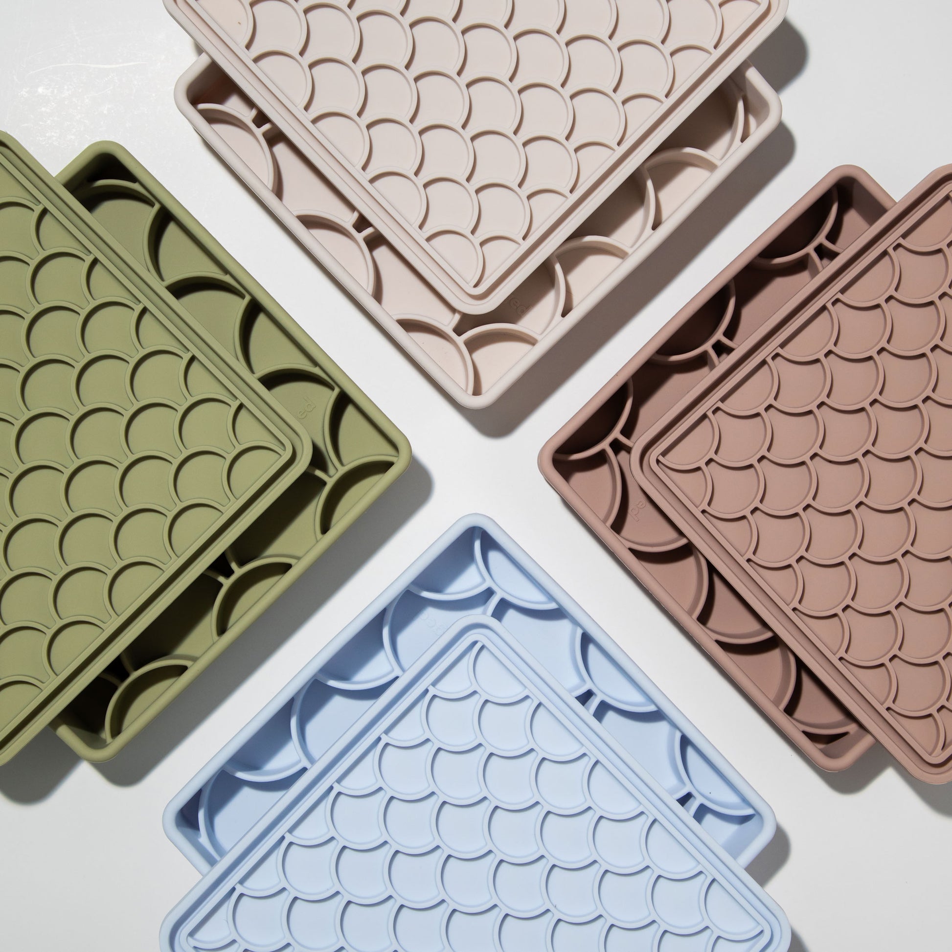 A flat lay of multiple 3-in-1 fish scale slow feeders in various colors, including fig, olive, sky, and sand, showcasing the range of color options.